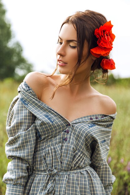 Portrait of a beautiful brunette woman in dress with red flowers in her hair in the field