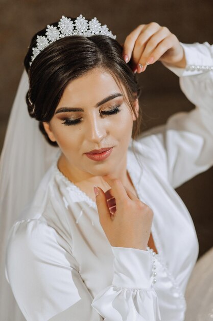 Portrait of a beautiful brunette woman in a glamorous silk wedding gown a crown on her head and a long veil Posing for a photographer