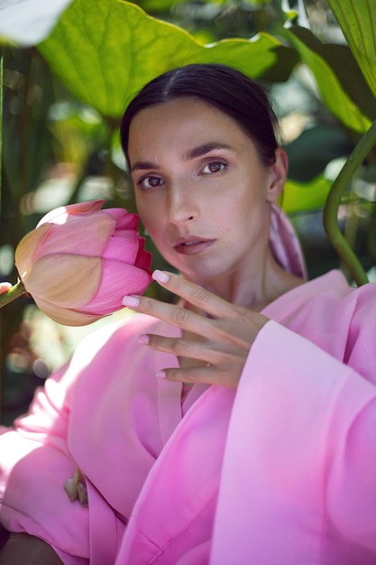 Portrait beautiful brunette woman in a pink dress is sitting on\
a boat among blooming lotuses on a lake in astrakhan