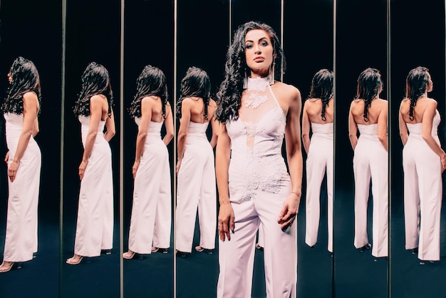 Portrait of beautiful brunette woman in white shoes and white pants suit standing near the mirrors