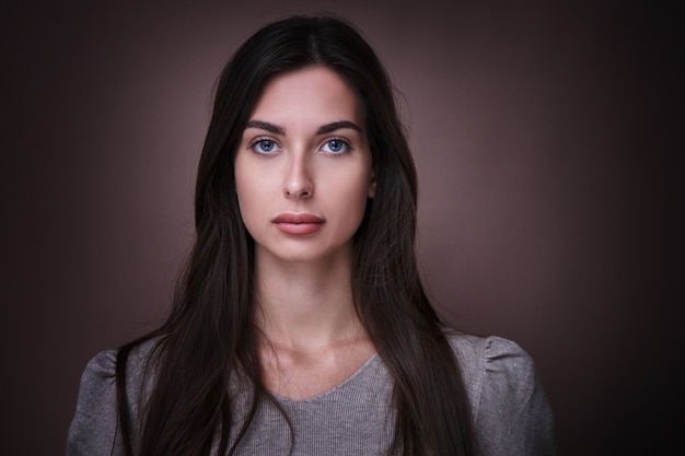 Ritratto di bella donna castana con espressione seria del viso isolato in sfondo marrone studio