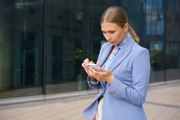 Portrait of a beautiful business woman in a blue jacket talking on the phone against the background of an office building