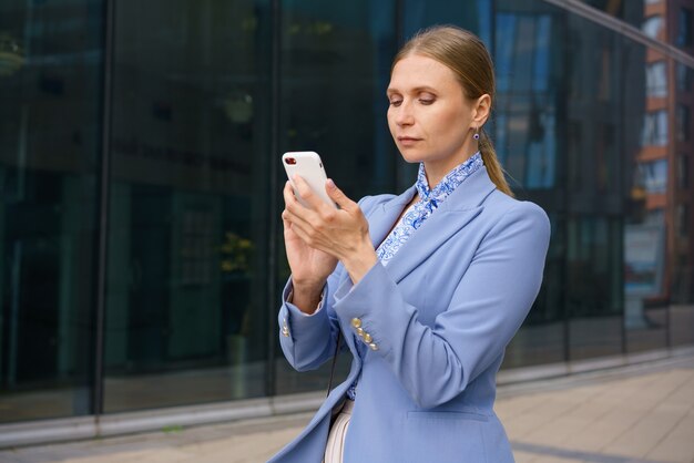 Portrait of a beautiful business woman in a blue jacket talking on the phone against the background of an office building