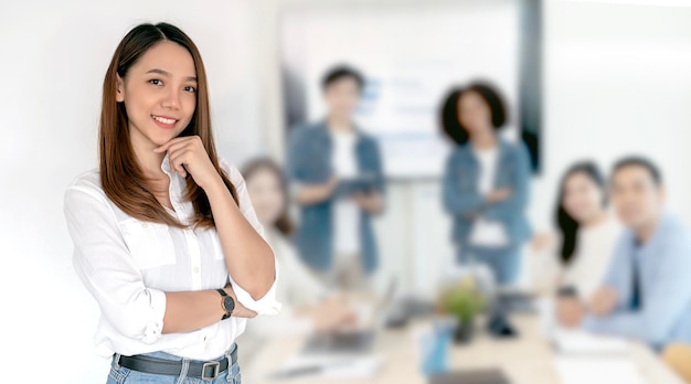 Portrait of beautiful businesswoman standing in meeting room with her colleagues in background