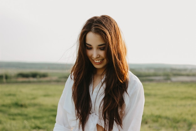 Portrait of beautiful carefree long hair girl in white clothes on field at sunset