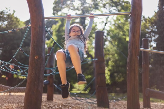 Photo portrait of a beautiful caucasian girl is doing push-ups on the horizontal bar in the the playgroun