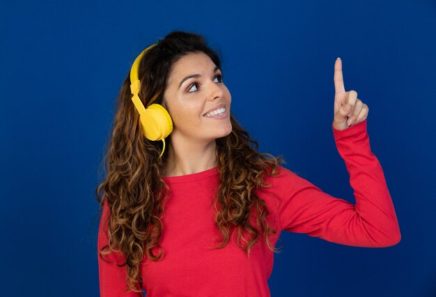 Portrait of beautiful caucasian girl with curly hair and headphones listening music isolated on a white wall