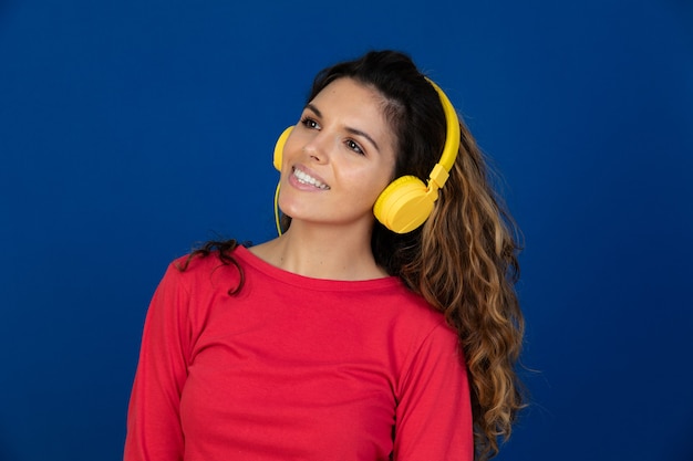 Portrait of beautiful caucasian girl with curly hair and headphones listening music isolated on a white wall