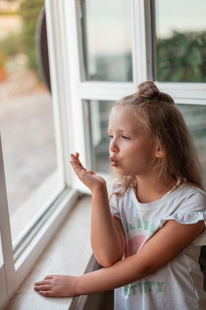 Portrait of a beautiful cheerful baby girl sending an air kiss at the window