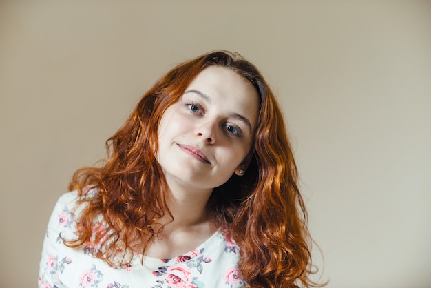 Portrait of beautiful cheerful redhead girl with curly hair over beige scene