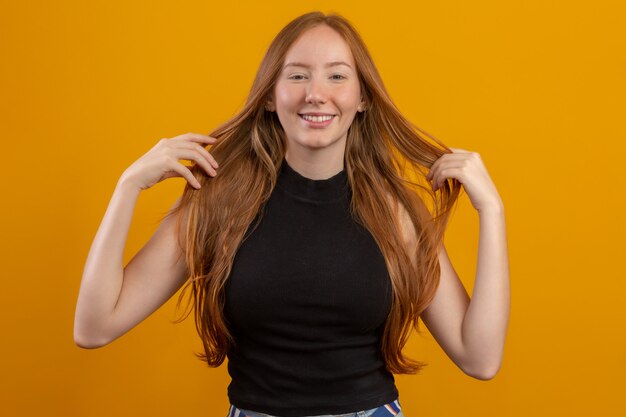 Портрет красивая веселая рыжая девушка с развевающимися волосами, улыбаясь, смеясь над желтой стеной.