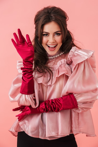 Portrait of a beautiful cheerful young brunette woman with bright makeup wearing fashionable clothes standing isolated over pink wall