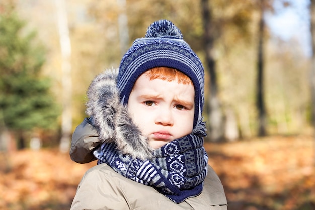 Portrait of a beautiful child with a upset expression on his face. The boy is dressed in warm clothes, autumn season. Photo closeup.