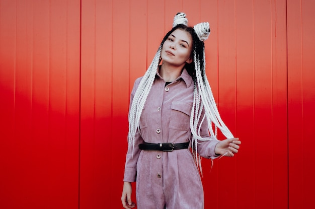 Portrait of beautiful cool girl with Senegalese pigtails and dreadlocks over red wall