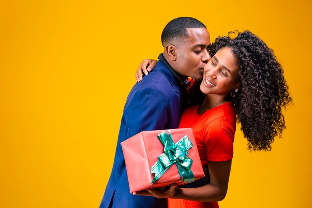 Portrait of a beautiful couple afro on yellow background holding a gift