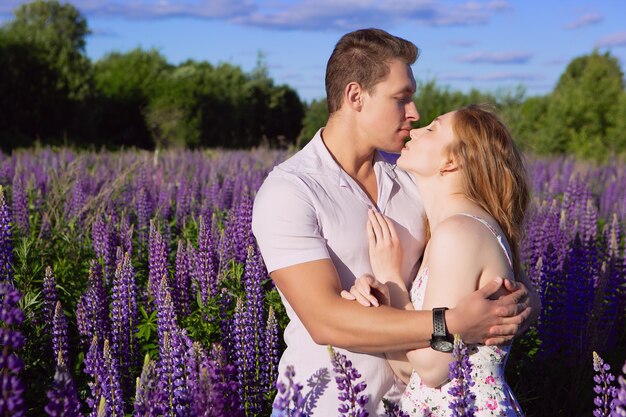 Portrait of a beautiful couple in love gently kissing on a blooming lupine field