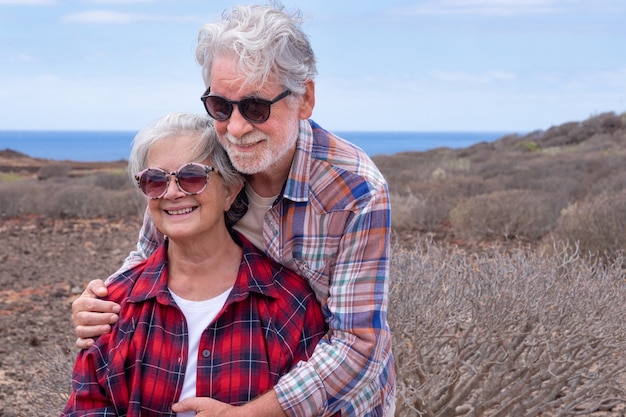 Portrait of beautiful couple of senior travelers in outdoors excursion in arid landscape.  Horizon over sea