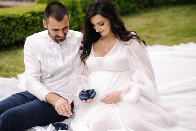 Portrait of beautiful couple sitting on a plaid on the grass elegant pregnant woman with husband