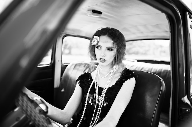 Portrait of beautiful curly fashion girl model with bright makeup in retro style sitting on a vintage car