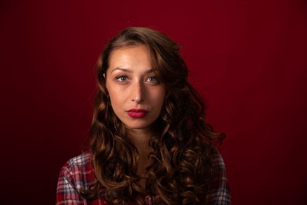 Ritratto di bello modello peloso lungo riccio in camicia a quadri in posa su studio rosso