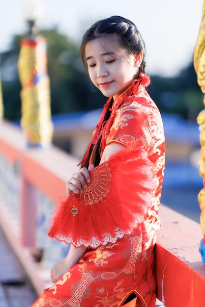 Ritratto bei sorrisi carini giovane donna asiatica che indossa la decorazione tradizionale cinese cheongsam rossa e tiene in mano un fanning cinese per il festival del capodanno cinese al santuario cinese in thailandia