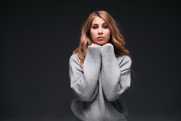 Portrait of beautiful cute woman model in casual gray sweater clothes on black wall