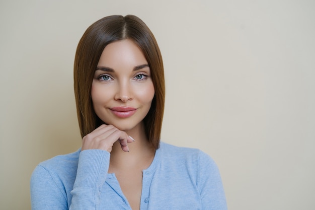 Ritratto di bella donna dai capelli scuri con pelle pulita naturale sana, tocca il mento