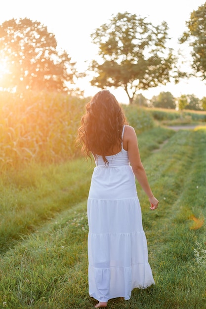 Portrait of a beautiful darkhaired curly young woman 30 years old in a white sundress in a summer field at sunset Beautiful summer model