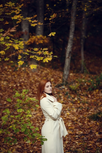 Portrait of a beautiful, dreamy and sad girl with red hair in white coat autumn