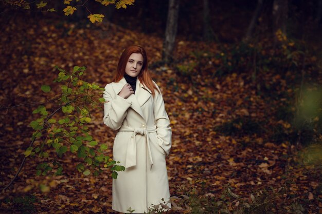 Portrait of a beautiful, dreamy and sad girl with red hair in white coat autumn