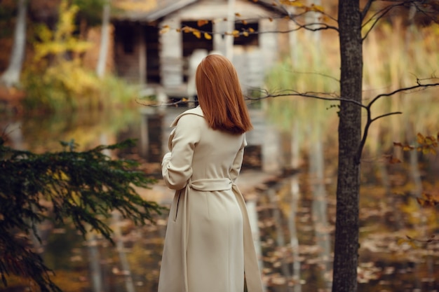 Ritratto di una ragazza bella, sognante e triste con i capelli rossi in camice bianco in autunno