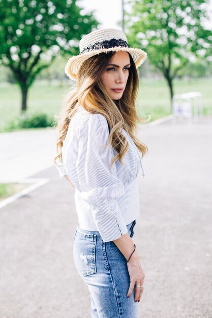 Portrait of a beautiful elegant woman with hat posing in the park at sunny summer day