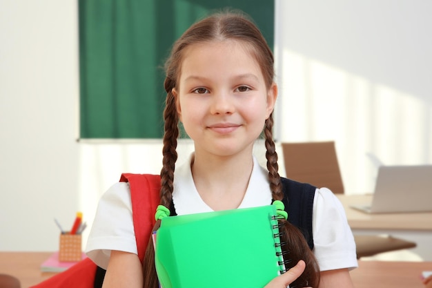 Photo portrait of beautiful elementary schoolgirl standing in classroom