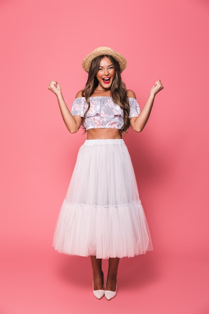 Portrait of beautiful excited woman wearing straw hat and fluffy skirt laughing while clenching fists like winner