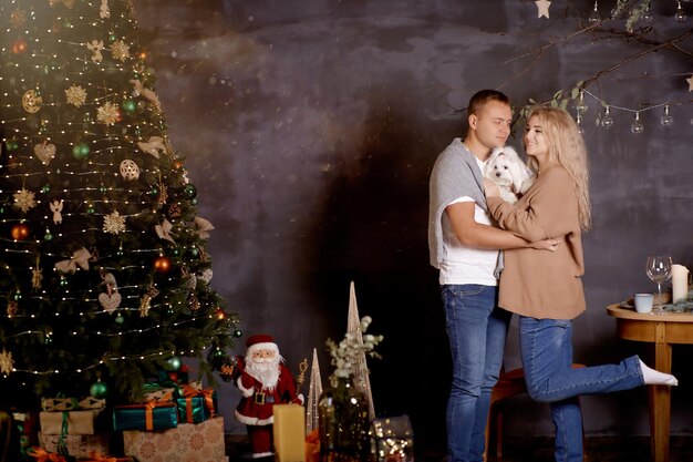 Portrait of beautiful family near Christmas tree Romantic couple with their dog near in festive aesthetic cozy home interior Good mood Christmas love story Candid true moment