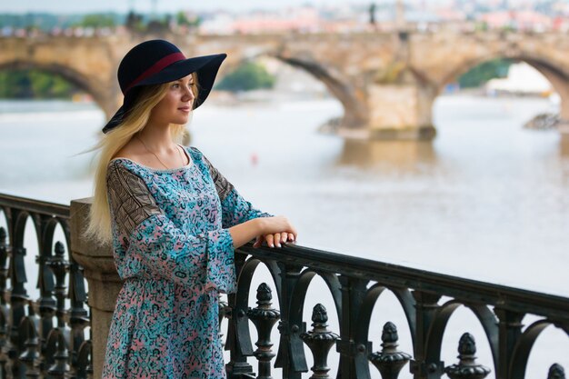 Portrait of the beautiful fashionable girl with hat on embankment in summer day