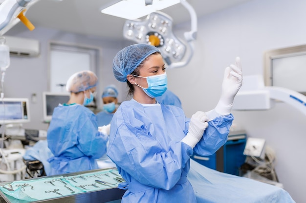 Portrait of beautiful female doctor surgeon putting on medical\
gloves standing in operation room surgeon at modern operating\
room