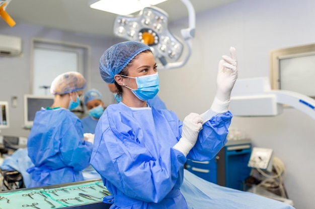 Portrait of beautiful female doctor surgeon putting on medical\
gloves standing in operation room surgeon at modern operating\
room