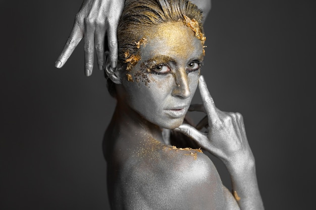 Portrait of a beautiful female model with gold and silver paint on her skin and hair in the studio.