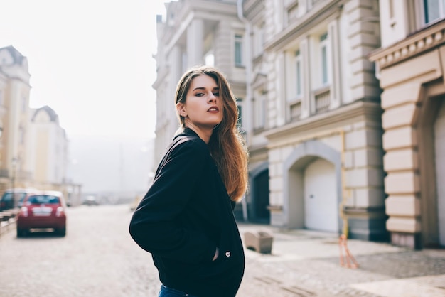 Портрет красивой студентки в черной куртке, проводящей свободное время во время прогулки по городу