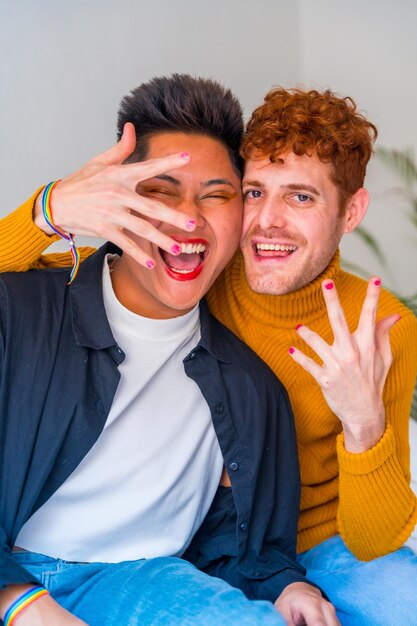 Portrait of beautiful gay couple putting on makeup with painted nails indoors at home lgbt concept