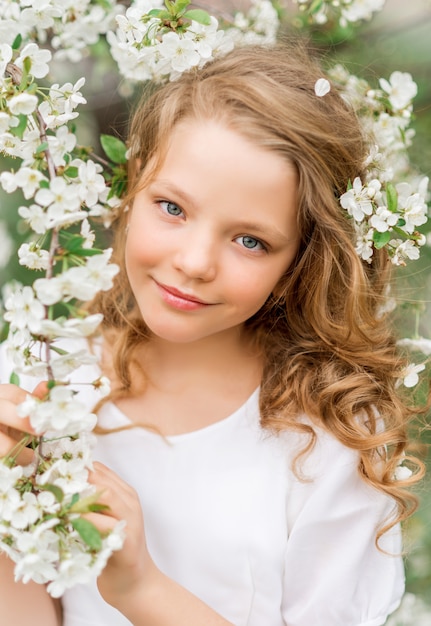 Portrait of a beautiful girl in a blooming garden in spring. Cute baby with white flowers in her hair.