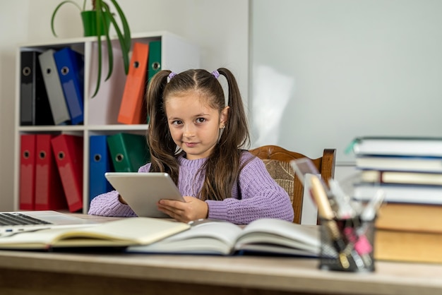 Portrait of a beautiful girl in the classroom at a desk with books and a computer