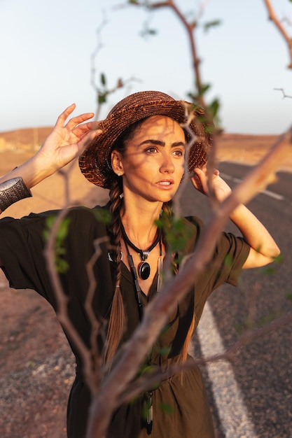 Portrait of a beautiful girl in a hat on the background of a road in the desert.