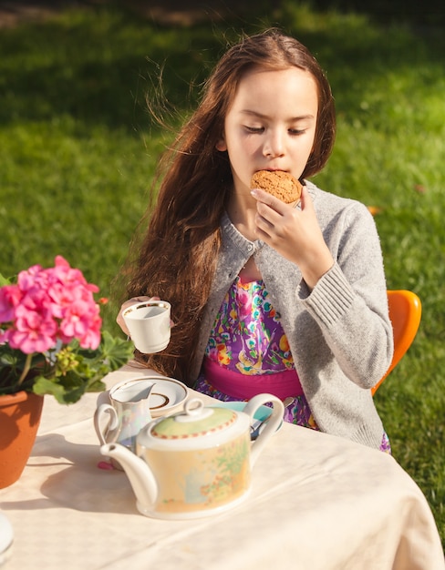 Portrait of beautiful girl having breakfast at yard and biting cookie