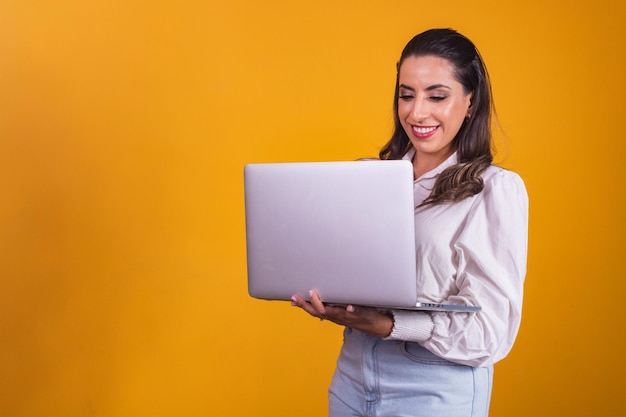 Portrait of beautiful girl holding a laptop in her hands. Young home office on yellow background working virtual with computer.