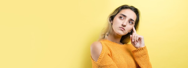 Portrait of a beautiful girl in an orange sweater looks aside with pensive expression is considering a plan for further action