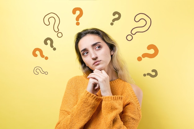 Portrait of a beautiful girl in an orange sweater looks aside with pensive expression is considering a plan for further action