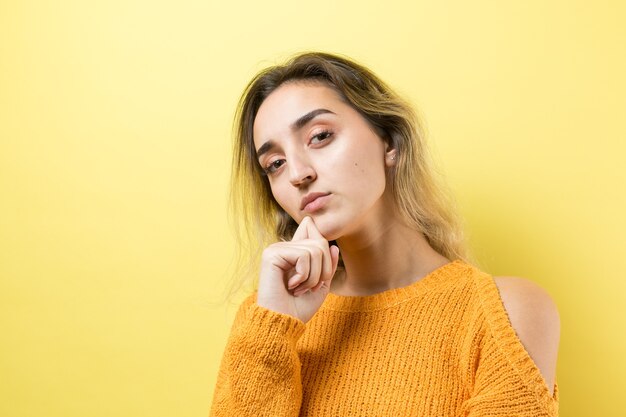 Portrait of a beautiful girl in an orange sweater looks aside with pensive expression