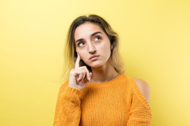 Portrait of a beautiful girl in an orange sweater looks aside with pensive expression